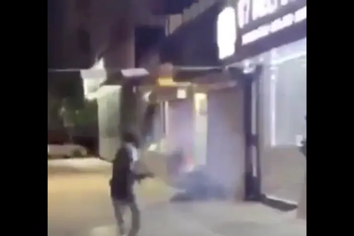 A screenshot from a video showing a man throwing a lit firework at someone who appears to be sleeping in NYC.